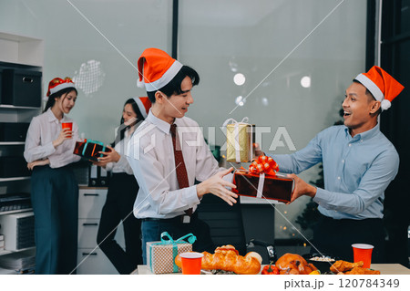 full length view of a group of business team wearing red Santa hat and exchange gift box together in the office for Christmas. 120784349