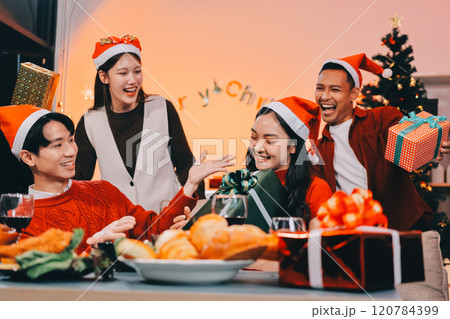 Group of young Asian man and women as friends having fun at a New Year's celebration, holding gift boxes standing by Christmas tree decoration, midnight countdown Party at home with holiday season. 120784399