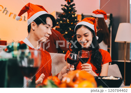Group of young Asian man and women as friends having fun at a New Year's celebration, holding gift boxes standing by Christmas tree decoration, midnight countdown Party at home with holiday season. 120784402