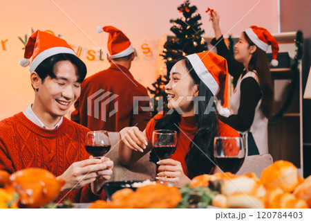 Group of young Asian man and women as friends having fun at a New Year's celebration, holding gift boxes standing by Christmas tree decoration, midnight countdown Party at home with holiday season. 120784403