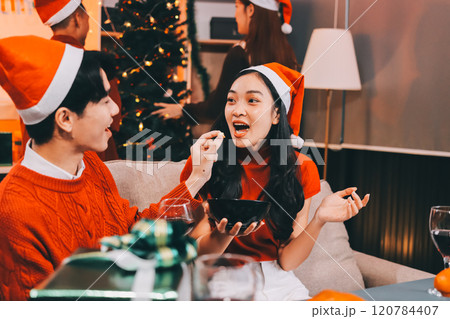 Group of young Asian man and women as friends having fun at a New Year's celebration, holding gift boxes standing by Christmas tree decoration, midnight countdown Party at home with holiday season. 120784407