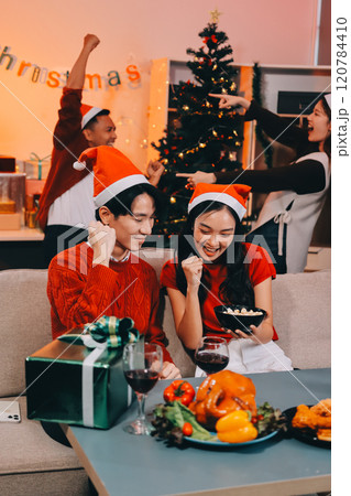 Group of young Asian man and women as friends having fun at a New Year's celebration, holding gift boxes standing by Christmas tree decoration, midnight countdown Party at home with holiday season. 120784410