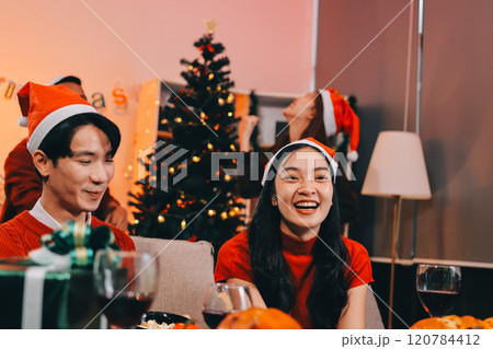 Group of young Asian man and women as friends having fun at a New Year's celebration, holding gift boxes standing by Christmas tree decoration, midnight countdown Party at home with holiday season. 120784412