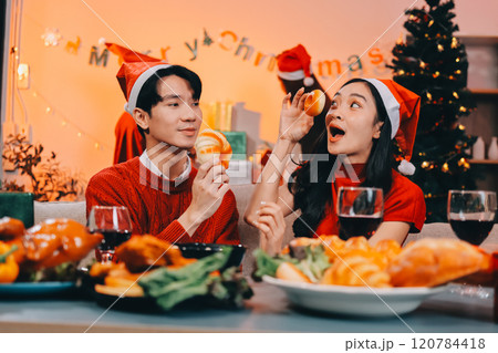 Group of young Asian man and women as friends having fun at a New Year's celebration, holding gift boxes standing by Christmas tree decoration, midnight countdown Party at home with holiday season. 120784418