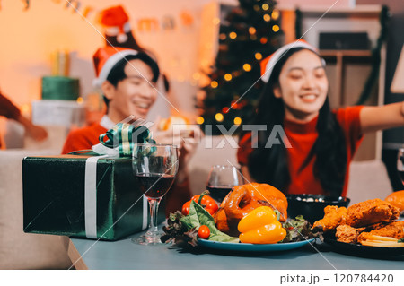 Group of young Asian man and women as friends having fun at a New Year's celebration, holding gift boxes standing by Christmas tree decoration, midnight countdown Party at home with holiday season. 120784420