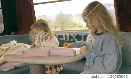 Two girls draw and write in the train during a long railroad trip in France Two girls draw and write in the train during a long railroad trip in France 120785668