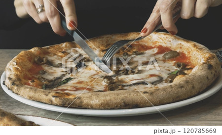 An elegant woman cuts freshly cooked hot pizza on her plate An elegant woman cuts freshly cooked hot pizza on her plate 120785669