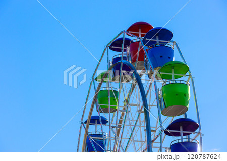 Colorful Ferris wheel with red, blue, green gondolas against bright blue sky. 120787624