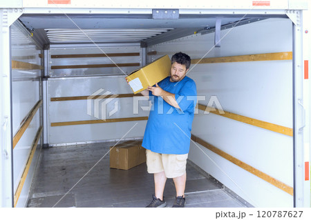 Man is lifting cardboard box while inside an empty moving truck features interior boxes are visible. Man is lifting cardboard box while inside an empty moving truck features interior boxes are visible. 120787627
