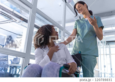 Dark-haired nurse carrying a wheelchair with a female patient 120789831