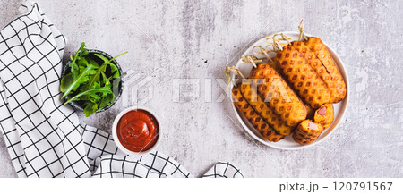 Grilled corn dogs with sausage on a plate and ketchup on the table top view web banner 120791567