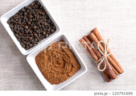 Cassia cinnamon powder and buds in white bowls, with cinnamon sticks tied together in a bundle, on linen fabric, and with empty space for text. Chinese cinnamon, Cinnamomum cassia, used as a spice. Cassia cinnamon powder and buds in white bowls, with cinnamon sticks tied together in a bundle, on linen fabric, and with empty space for text. Chinese cinnamon, Cinnamomum cassia, used as a spice. 120791899