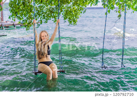 Beautiful female tourist relaxing on a swing in Laguna Bacalar in Mexico during kayak trip. Female tourist swinging over Lake Bacalar with feet in the water. Quintana Roo, Mexico travel, relaxation 120792710