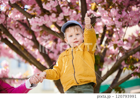 Young boy allergic enjoying after treatment from seasonal allergy at spring. Portrait of happy guy smiling, showing thumbs up gesture in front of blooming tree at springtime. Spring allergy concept. 120793991