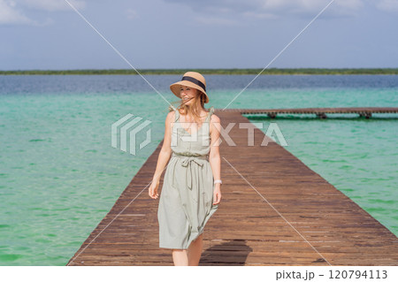 Female tourist in a turquoise dress standing on a wooden pier over the turquoise waters of Bacalar Lake, Mexico. Peaceful tropical travel destination concept Female tourist in a turquoise dress standing on a wooden pier over the turquoise waters of Bacalar Lake, Mexico. Peaceful tropical travel destination concept 120794113
