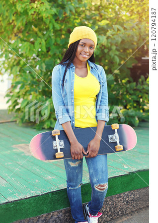 Portrait of happy smiling young african woman model posing with skateboard in the city Portrait of happy smiling young african woman model posing with skateboard in the city 120794187