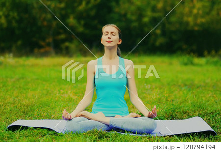 Young woman doing yoga exercises on a mat on the grass in summer park 120794194