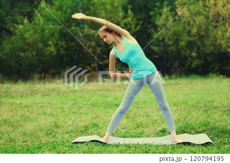 Fitness woman doing yoga exercises on a mat on the grass in summer park 120794195