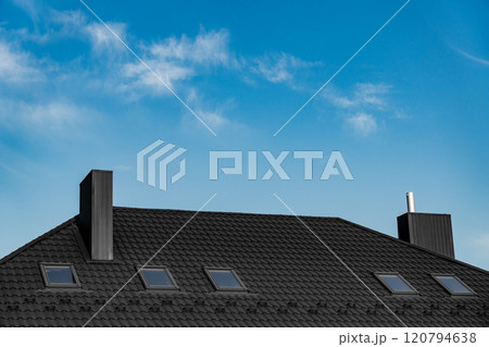 A modern house with a black tiled roof showcases several skylights against a bright blue sky. The daylight highlights the architecture and roofing design A modern house with a black tiled roof showcases several skylights against a bright blue sky. The daylight highlights the architecture and roofing design 120794638