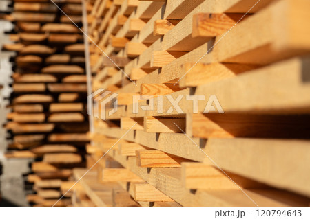 Wooden boards are neatly stacked in a lumber yard, illuminated by the warm light of golden hour, highlighting the beauty of natural wood and craftsmanship in construction 120794643