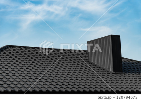 Roof of house is covered with black metal modern roofing material against the sky. Corrugated metal roof and metal roofing Roof of house is covered with black metal modern roofing material against the sky. Corrugated metal roof and metal roofing 120794675