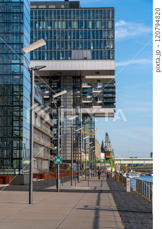 Modern riverside building with a unique architectural design reflects on the calm water under a clear blue sky. The warm sunlight highlights its structure and nearby surroundings. Landscape of Cologne 120794820