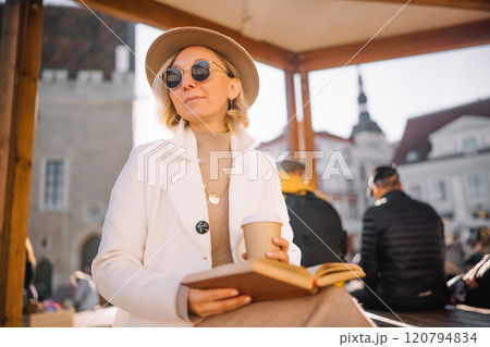 Woman enjoying a book and coffee in a cozy outdoor setting at a town square 120794834
