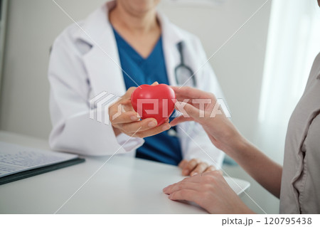 A doctor is holding a red heart in front of a patient 120795438