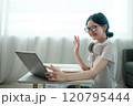 A woman wearing glasses and headphones is sitting at a table with a laptop open 120795444
