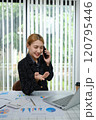 A woman is talking on her cell phone while sitting at a desk with a laptop 120795446