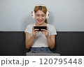A woman is sitting on a couch and playing a game on her phone 120795448
