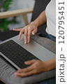 A woman is sitting on a couch with a laptop on her lap 120795451