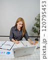 A woman is sitting at a desk with a laptop and a notebook 120795453