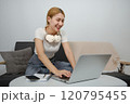 A woman is sitting on a couch and using a laptop 120795455