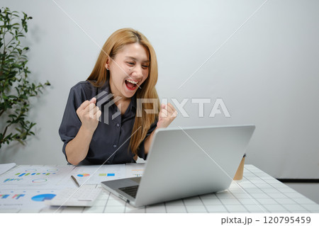 A woman is sitting at a desk with a laptop open and a smile on her face 120795459
