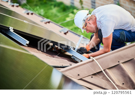Worker building photovoltaic solar panel system on rooftop of house. Man using ruler to measure mounting equipment for precise installation for generating electricity through photovoltaic effect. Worker building photovoltaic solar panel system on rooftop of house. Man using ruler to measure mounting equipment for precise installation for generating electricity through photovoltaic effect. 120795561