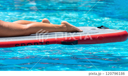 Close-up of legs on a paddleboard in a tropical pool. Concept of aquatic relaxation and fitness Close-up of legs on a paddleboard in a tropical pool. Concept of aquatic relaxation and fitness 120796186