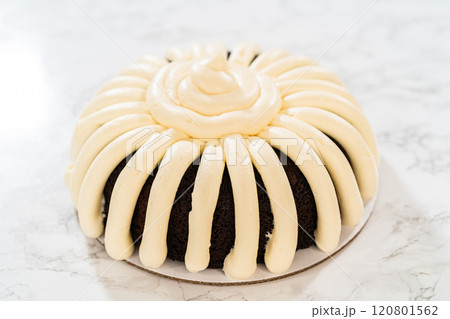 With precision, the Chocolate Bundt Cake is carefully removed from the pan - adorned with luscious cream cheese frosting, creating a delectable treat that is sure to delight. 120801562