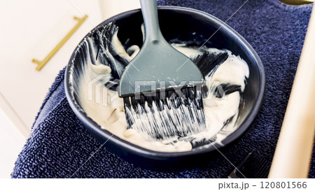 Rich, creamy hair dye mix rests on a wooden brush over a sleek bowl. The tools for hair coloring lie on a dark, textured towel, with a hint of vibrant pink peeking through, suggesting the lively work 120801566