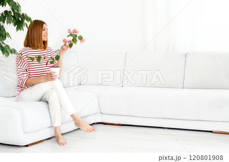 girl with a plant in a pot. Smiling real woman at home. White interior. Copy space 120801908