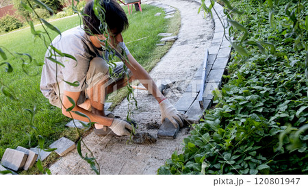 Young men is laying paving stones on cement mortar. Laying a garden path made of tiles. Self-laying of concrete paving slabs in the courtyard of the house. do it yourself. DIY 120801947