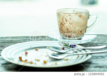 Empty coffee cup with stained interior and empty dessert plate with crumbs and utensils, placed on rustic wooden table near window light Empty coffee cup with stained interior and empty dessert plate with crumbs and utensils, placed on rustic wooden table near window light 120804092