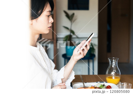スマホを見ながら朝食を食べる女性 120805080