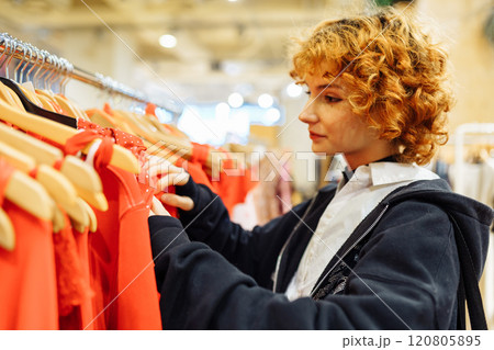 young attractive red-haired woman choosing red clothes in boutique 120805895