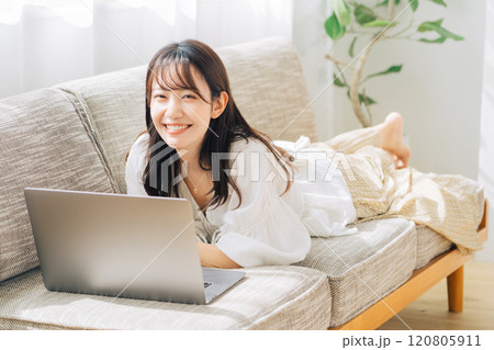 ソファで寝転がりながらパソコンを使う女性 120805911