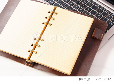 リング式のシステム手帳を開いて、ノートパソコンでデスクワークをしているイメージ 120807232