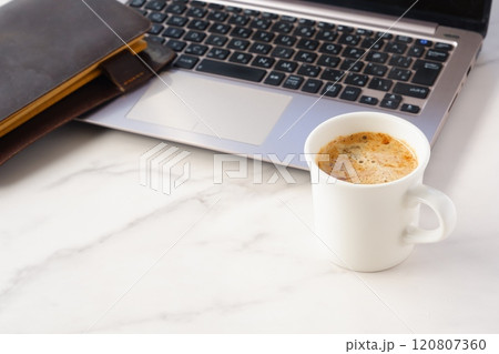 淹れたての美味しいコーヒーを飲みながら、ノートパソコンとシステム手帳でデスクワークをしているイメージ 120807360