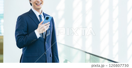 オフィスビルのロビーでスマホを使う男性ビジネスパーソン オフィスビルのロビーでスマホを使う男性ビジネスパーソン 120807730