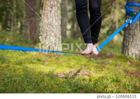 Close-up of feet balancing on a slackline in a lush forest setting 120808215