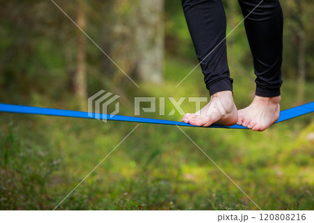 Close-up of feet balancing on a slackline in a lush forest setting 120808216
